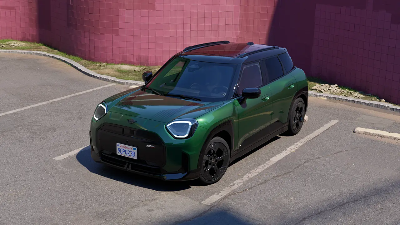 Vue frontale du stationnement de la MINI Aceman 100 % électrique en British Racing Green dans le parking avec un mur rose en l'arrière-plan