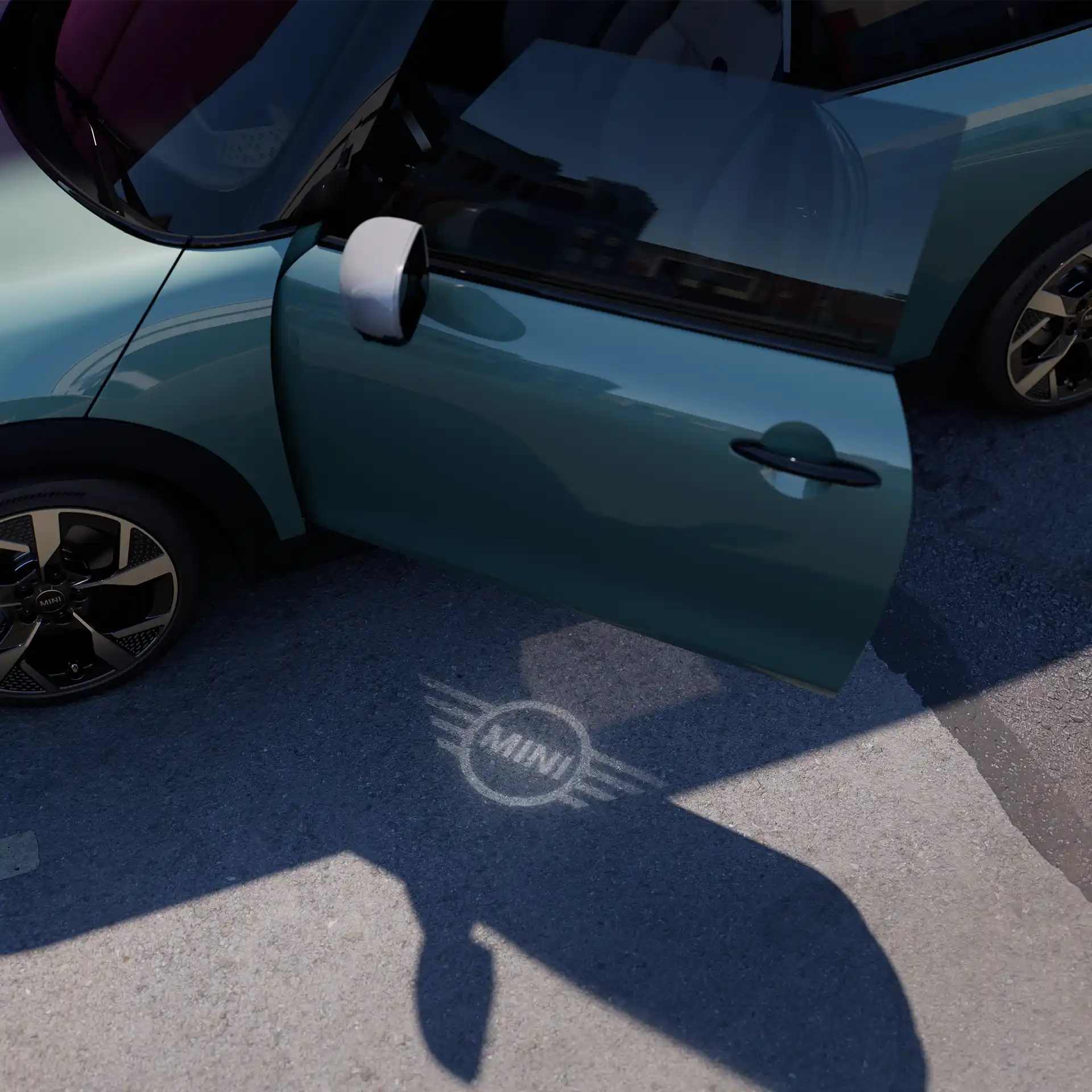 Vue extérieure d’une MINI Cooper avec portière ouverte et projection de bienvenue avec logo MINI sur le sol 