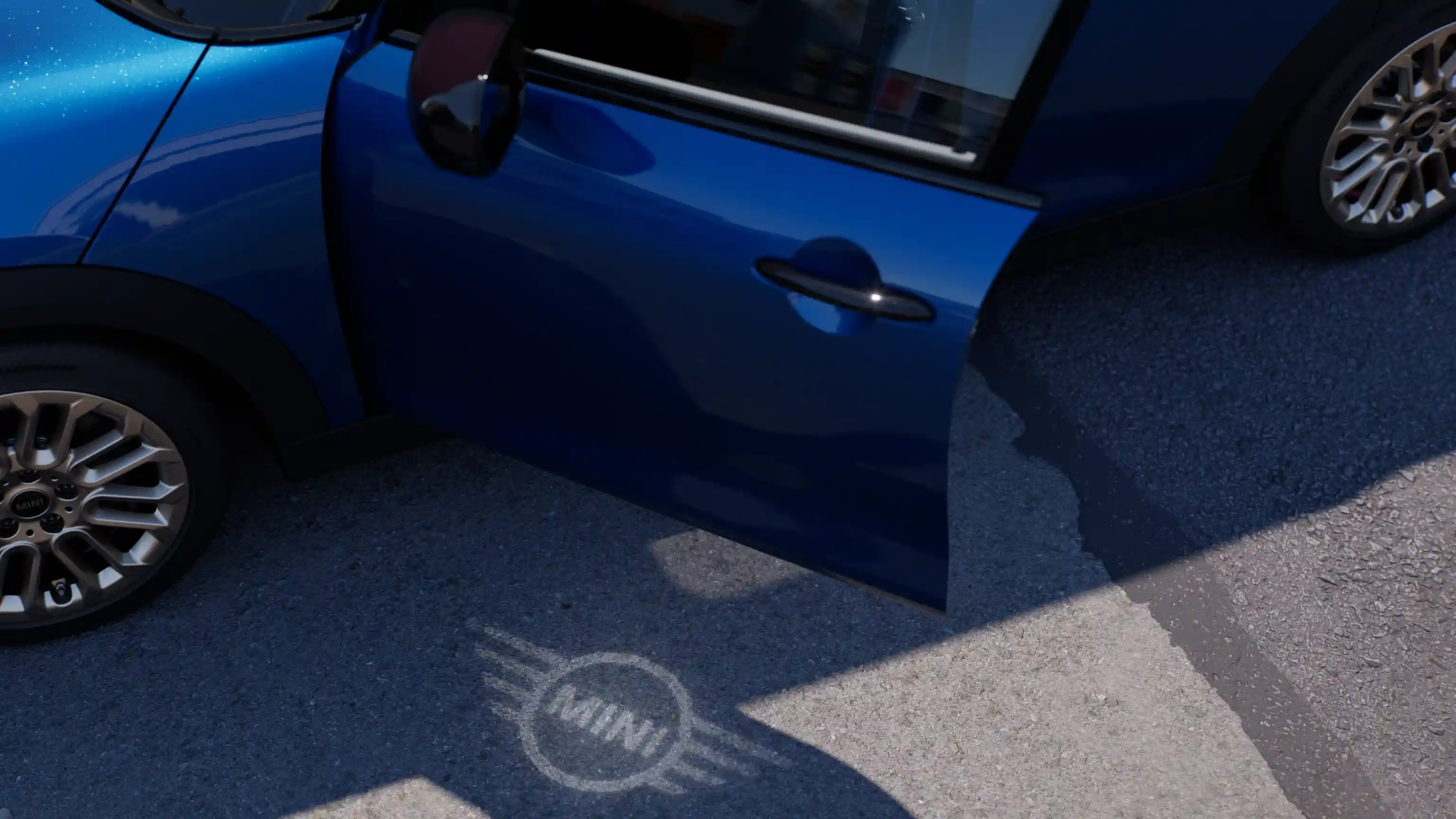 Buitenkant van de MINI Cooper 5-deurs met open deur en MINI logo dat op de grond oplicht