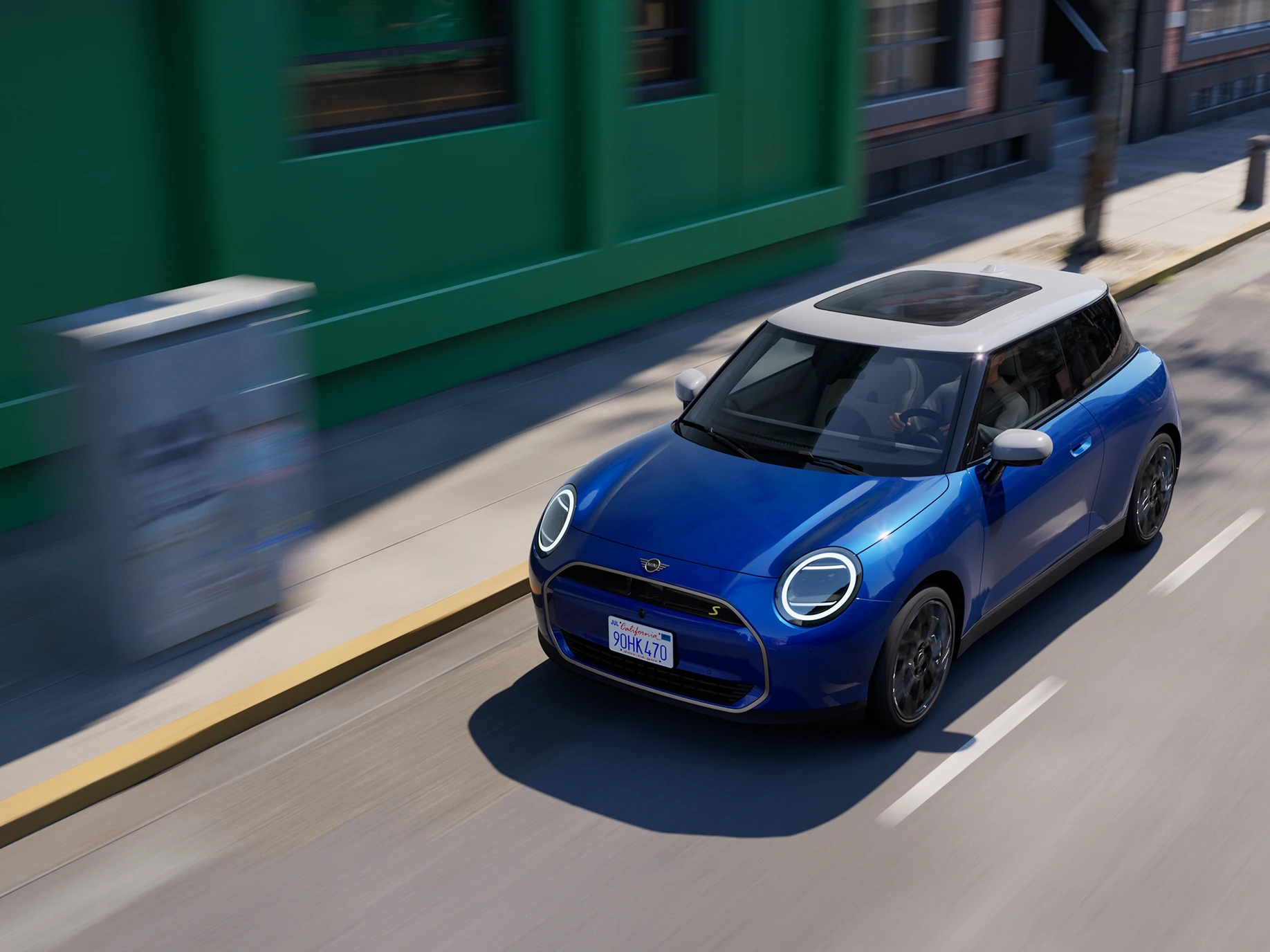 Bovenaanzicht van de MINI Cooper Electric in Blazing Blue and White Roof die op straat rijdt. 