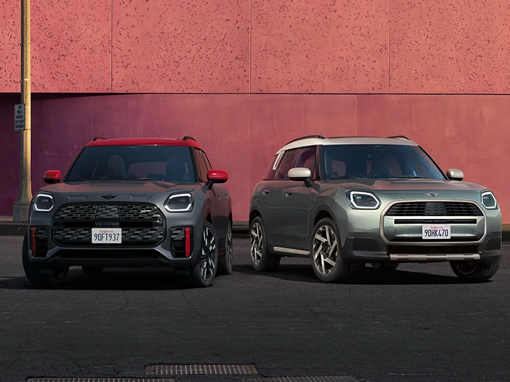 Vue de face de la MINI Countryman JCW Legend Grey avec toit rouge et de la MINI Countryman Smokey Green avec toit Vibrant Silver, stationnées côte-à-côte.