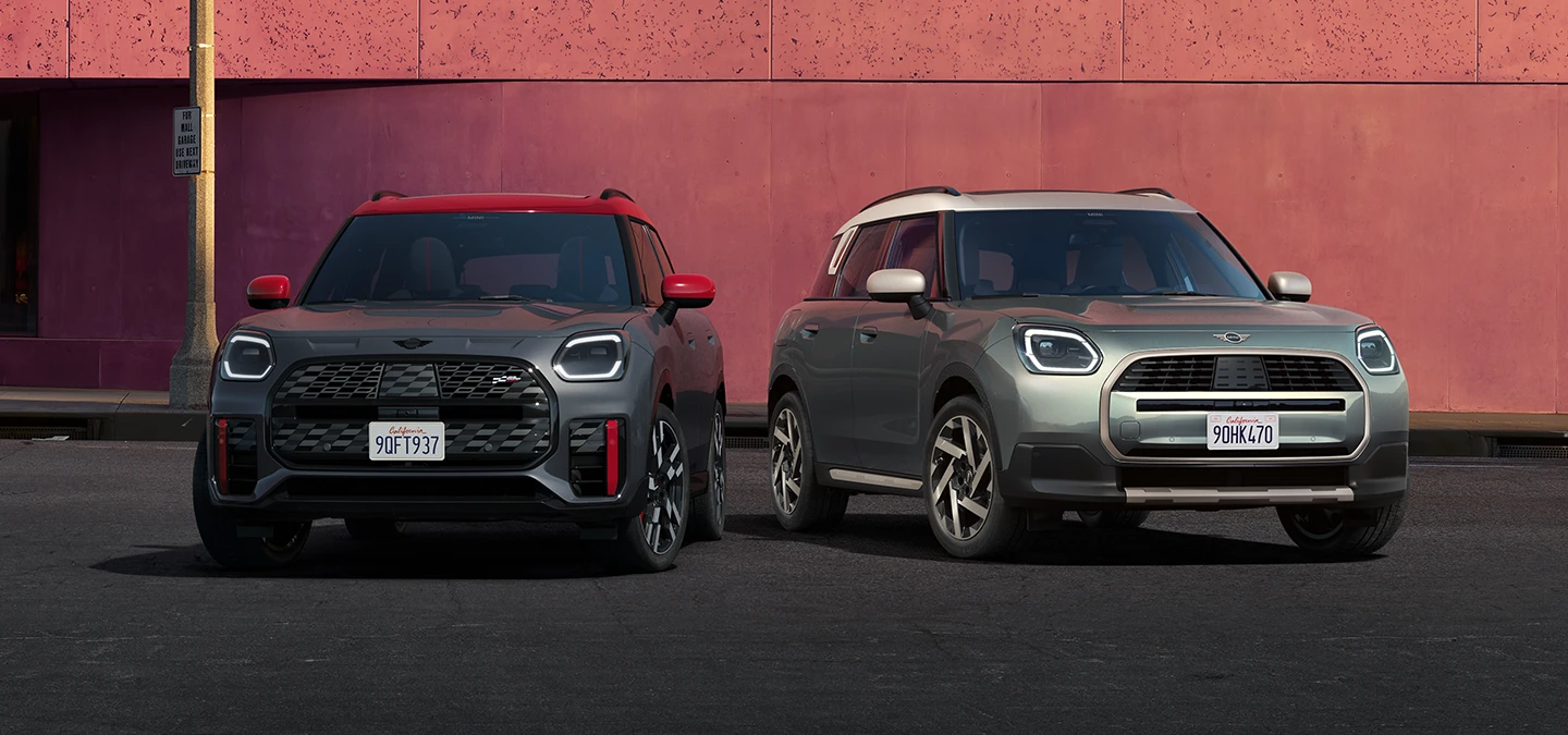 Vue de face de la MINI Countryman JCW Legend Grey avec toit rouge et de la MINI Countryman Smokey Green avec toit Vibrant Silver, stationnées côte-à-côte.
