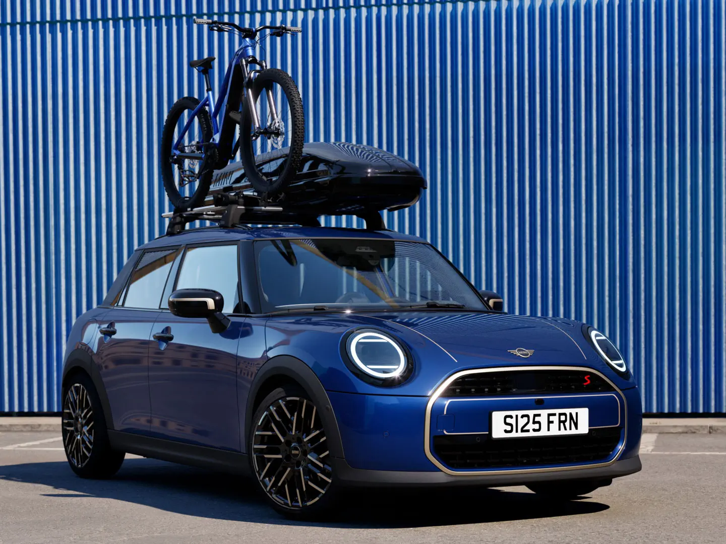 Vue de face de la MINI Aceman en Indigo Sunset Blue avec porte-vélos de toit MINI, transportant un vélo de montagne et un coffre de toit MINI 320.