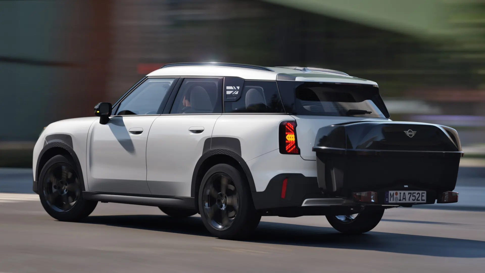 Vue latérale arrière de la MINI Aceman en Nanuq White équipée d'un porte-vélos arrière MINI et transportant le compartiment arrière MINI. 