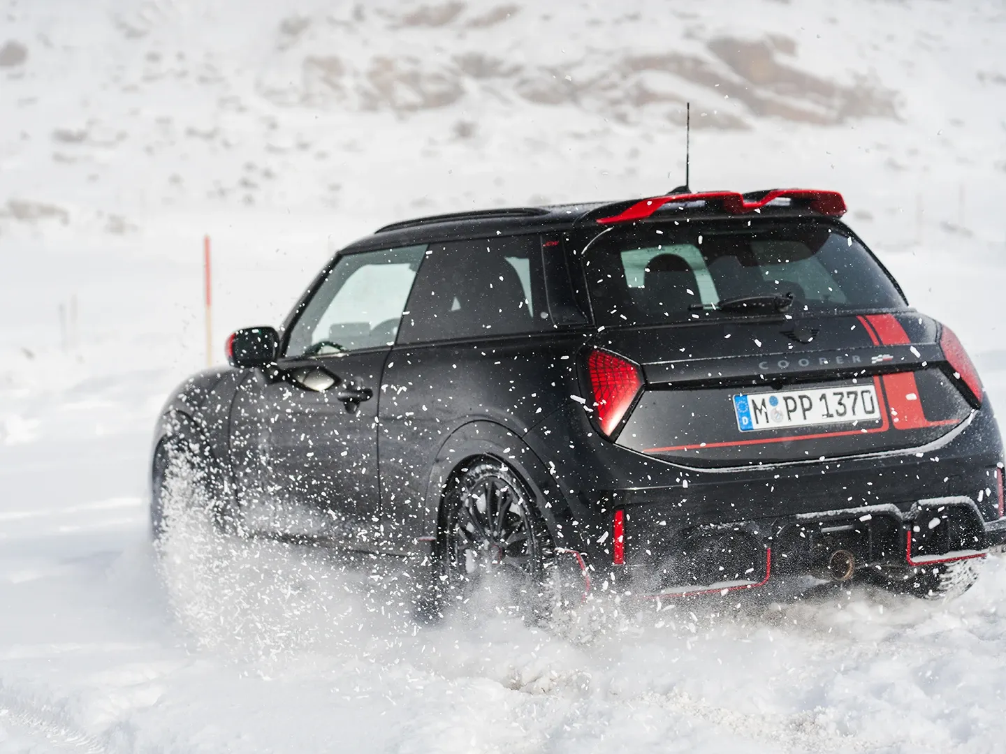 Vue arrière d'une MINI Cooper JCW roulant dans la neige.