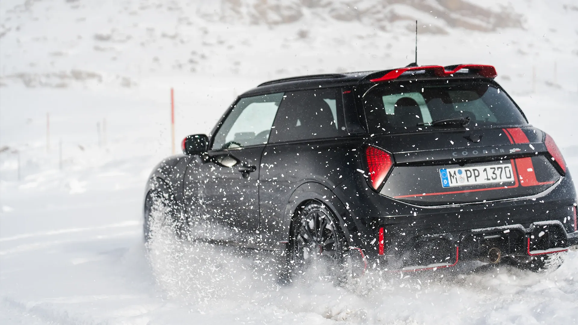 Vue arrière d'une MINI Cooper JCW roulant dans la neige.