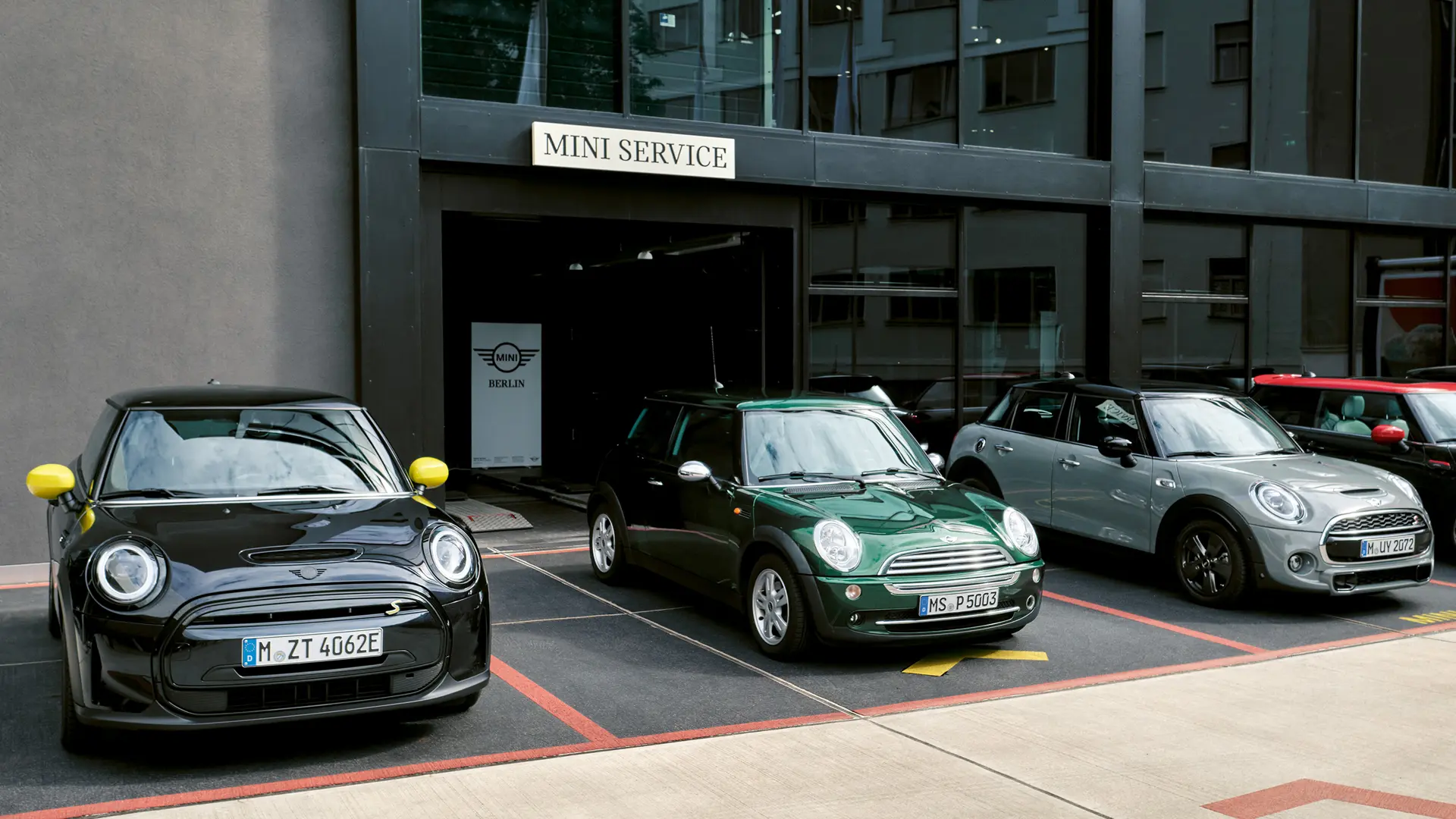 MINI Cooper Electric S noire garée devant une concession MINI, à côté d’une MINI Cooper 3 portes verte, d’une MINI 5 portes argent et d’une MINI JCW noire, vue de face. 