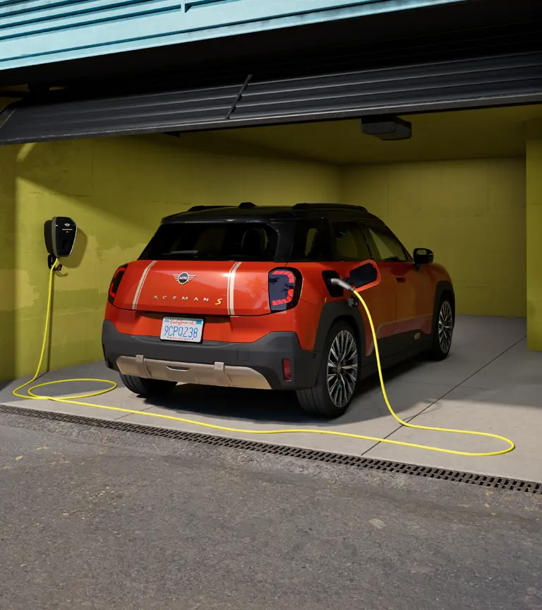 MINI Aceman S 100 % électrique stationné dans un garage, en cours de recharge avec la MINI Wallbox Plus, vue arrière.
